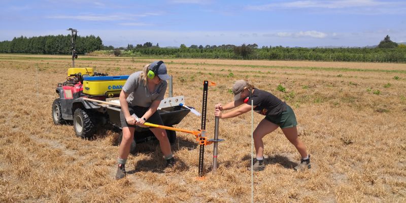 Two people using jack to lift soil coring tube out of the ground